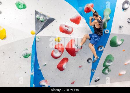 Stock Foto von einem erwachsenen Mann klettern drinnen. Er trägt ein schwarzes Tanktop und blaue Shorts. Er ist nicht erkennbar. Stockfoto