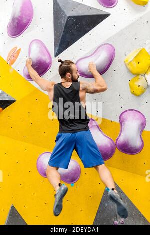 Stock Foto von einem erwachsenen Mann klettern drinnen. Er trägt ein schwarzes Tanktop und blaue Shorts. Er ist nicht erkennbar. Stockfoto