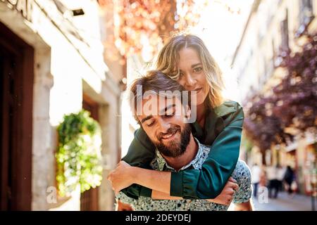 Stock Foto von einem Paar in ihren 30ern. Die Frau ist auf dem mans Rücken. Sie schauen auf die Kamera. Sie tragen legeres Tuch. Stockfoto