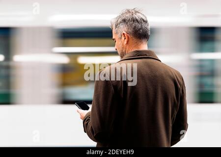 Stock Foto von einem Geschäftsmann tippen in seinem Smartphone warten, um die U-Bahn in der Plattform nehmen. Er ist nicht erkennbar. Stockfoto