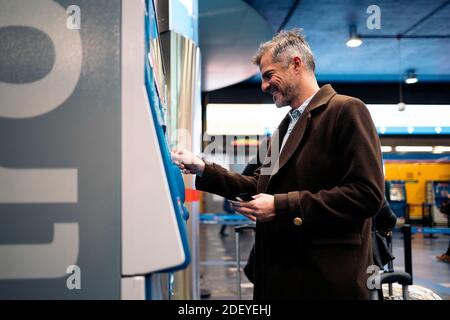 Stock-Foto von einer Seitenansicht eines kaukasischen Geschäftsmanns, der ein U-Bahnticket am Bahnhofsautomaten kauft. Er lächelt. Stockfoto