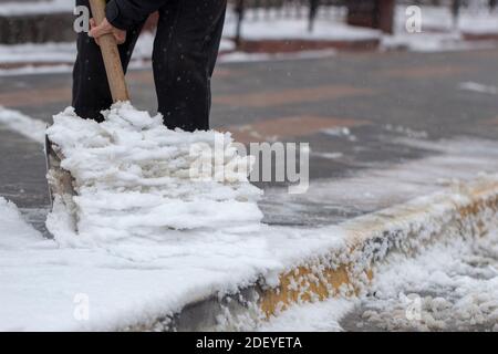 Mann mit Schneeschaufel reinigt Gehwege in Winterstraße. Stockfoto