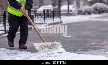 Mann mit Schneeschaufel reinigt Gehwege in Winterstraße. Stockfoto