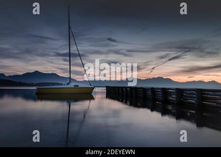 Gelbes Boot am Abend am Chiemsee mit glattem Wasser. Stockfoto