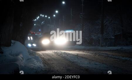 Schöne ländliche Winter schneebedeckte Straße mit Laternen an. Und leichte Wege von Autos Stockfoto