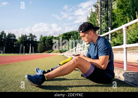 Behinderter Mann Athlet mit seinem Handy, während im Gras sitzen. Stockfoto