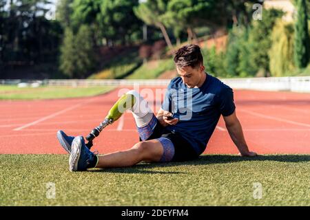 Behinderter Mann Athlet mit seinem Handy, während im Gras sitzen. Stockfoto
