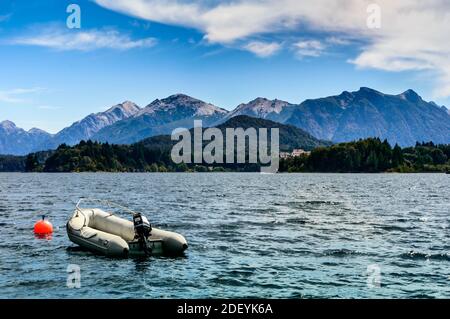 Seeufer mit Felsen, Bergen und Pinien. Ein Motorboot, das in der Nähe einer Boje schwimmt. Sommer in Bariloche. Stockfoto