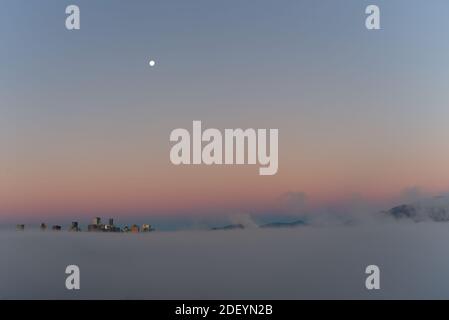 Stadt in der Wolke Mond im Hintergrund, Vancouver City Wolkenkratzer über dem Nebel mit der Morgensonne Schaffung reflektierenden falschen Sonnenuntergang Seite des Mondes Stockfoto