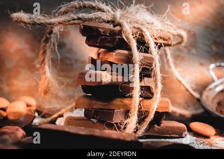 Stapel von Milch und dunkle Schokolade Stücke zusammen mit Garn und Bogen atmosphärischen Vorderansicht Foto gebunden. Stockfoto