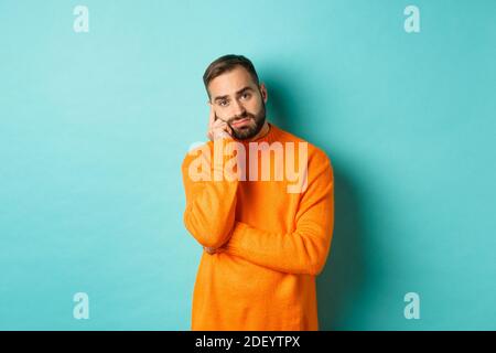 Trauriger und düsterer Mann mit Bart, unvoreinlich und traurig, über etwas nachdenkend und schmollend, über türkisfarbenem Hintergrund stehend Stockfoto
