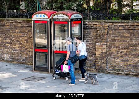 London, Großbritannien - 22. Juni 2018: Ehrliche Menschen, die auf der Straße auf dem Bürgersteig an der alten roten Telefonzelle und der Wand vorbeigehen Stockfoto