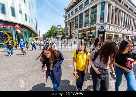 London, Großbritannien - 24. Juni 2018: Menschen überqueren den Fußgängerüberweg am Leicester Square durch M&MS Candy Store und TWG Tea Shop für Uhr und internationale Flaggen in Soh Stockfoto