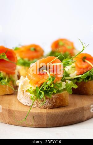 Kanapees mit Mozzarella-Käse, Salat, Lachs und Erbsensprossen, Toast mit rotem Fisch auf einem Holzbrett aus nächster Nähe Stockfoto