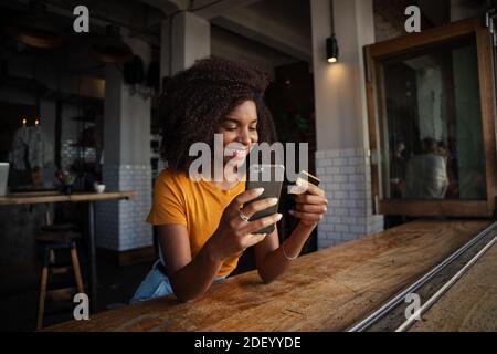Schöner Kunde hält Smartphone SMS Freunde, während bereit zu machen Bezahlung für leckeren Kaffee im trendigen Café Stockfoto