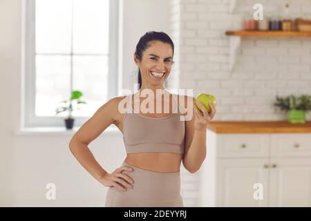 Fit Frau steht in der Küche, hält frischen grünen Apfel und lächelt an der Kamera Stockfoto