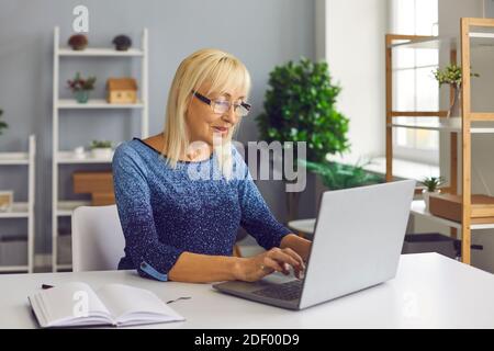 Inspirierte reife Frau, die am Laptop arbeitet, Buch schreibt oder Artikel auf ihrem Blog veröffentlicht Stockfoto