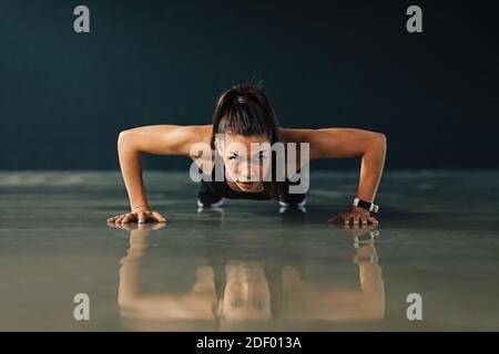 Frau in Sportbekleidung Training drinnen. Starke junge Frau tun Liegestützen und Blick auf die Kamera. Stockfoto