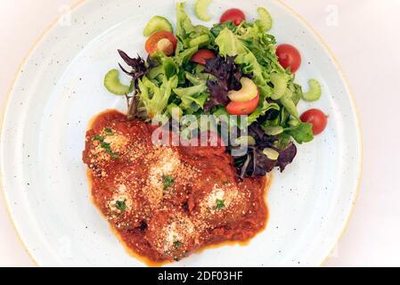 Blick von oben auf authentische italienische Küche zeigt nahrhafte Polpettine Fleischbällchen mit Marinara-Sauce und Salat auf einem Teller und bereit zu essen bedeckt. Stockfoto