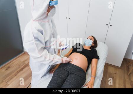 Ein Gynäkologe untersucht eine schwangere Frau während einer Covid 19 Pandemie. Fetale doppler-Herzauskultation. Stockfoto