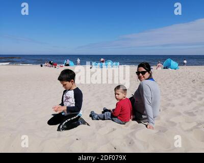 POBIEROWO, POLEN - 15. Jun 2020: Frau, die an einem warmen Frühlingstag mit zwei Kindern auf Sand am Strand sitzt Stockfoto