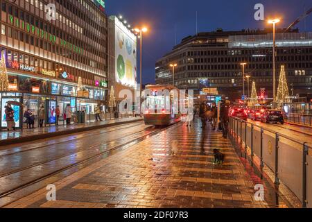 Helsinki, Finnland 30. November 2020 Stadtzentrum, historische Gebäude und eine vorbeifahrende grüne Straßenbahn. Brennende Laternen und Reflexionen nach dem Regen. Hochwertige Fotos Stockfoto