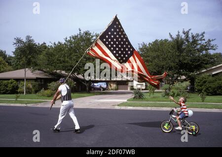 Junge Reiten kleines Fahrrad mit Training Räder greift für amerikanische Flagge während der Feier am 4. Juli in Austin, TX. ©Bob Daemmrich Stockfoto