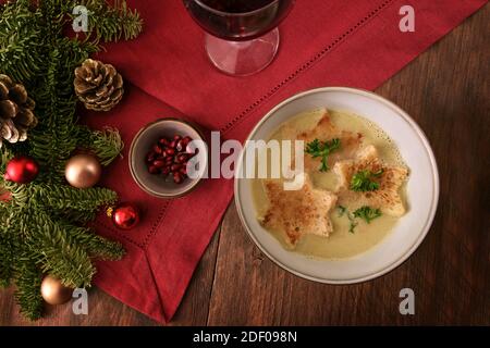 Sahnesuppe mit Croutons in Sternform, Petersiliengarnitur und Granatapfelkernen, Weihnachtsdekoration und einer roten Serviette auf einem dunklen rustikalen Holztisch, Hi Stockfoto