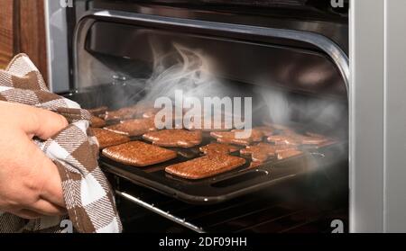 Hand herausnehmen Weihnachten Lebkuchenkekse aus offenen dampfenden Küche Ofen. Traditionelle Weihnachts- und Neujahrsgebäck vorbereiten. Heißer, leicht verbrannter Kuchen. Stockfoto