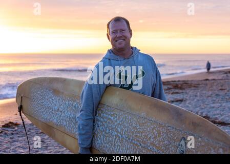 Florida Surfer mit Longboard am Strand nach einem Sonnenaufgang Surf Session bei Mickler's Landing in Ponte Vedra Beach, Florida. (USA) Stockfoto