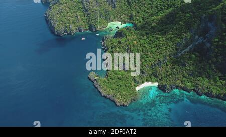 Top down grüne bergige Insel in Ocean Bay in Luftaufnahme. Kleine Passagierboote an der Küste Meerwasser. Tropische Naturlandschaft mit weißem Sandstrand von Palawan Island, Philippinen, Asien Stockfoto
