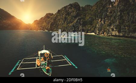 Seascape mit Passagierbooten bei Sonnenuntergang in Nahaufnahme Luftaufnahme. Cliff Coast mit grünen Bäumen an sonnigen Sommertagen. Philippinen Urlaub mit Touristen schwimmen am Meer Wasser. Sun set filmische Drohne aufgenommen Stockfoto