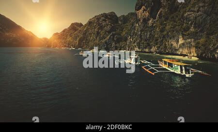 Seascape mit Passagierbooten bei Sonnenuntergang in Nahaufnahme Luftaufnahme. Cliff Coast mit grünen Bäumen an sonnigen Sommertagen. Philippinen Urlaub mit Touristen schwimmen am Meer Wasser. Sun set filmische Drohne aufgenommen Stockfoto