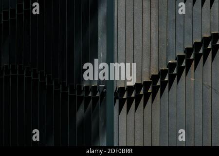 Fragment eines schwarzen Zauns aus Stahlbändern, die von der Seite von der Sonne beleuchtet werden. Taschen aus Rost auf Metall. Abstraktes Bild. Speicherplatz kopieren. Stockfoto