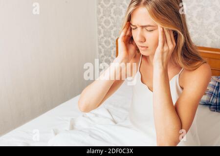 Junge schöne Mädchen sitzt in Pyjamas auf dem Bett in ihrem Zimmer, und drückt ihre Hände auf den Kopf Gefühl, starke Kopfschmerzen Stockfoto