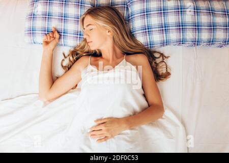Junge schöne Mädchen schlafen im Bett. Porträt einer Frau, die sich morgens auf einem bequemen Bett mit Kissen und weißem Bettzeug ausruhen. Stockfoto