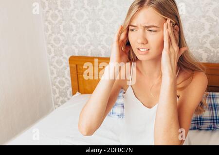 Junge schöne Mädchen sitzt in Pyjamas auf dem Bett in ihrem Zimmer, und drückt ihre Hände auf den Kopf Gefühl, starke Kopfschmerzen Stockfoto