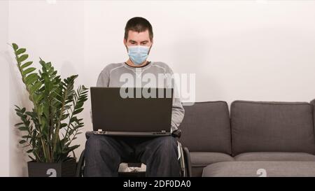 Mann im Rollstuhl, der von zu Hause aus mit einem Laptop arbeitet und mit einem virtuellen Web-Chat auf den Bildschirm schaut. Stockfoto