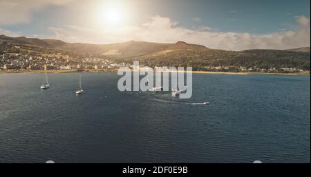 Luftaufnahme von Luxusyacht, Segel-Motorboot auf Meeresbucht. Sommerurlaub auf Booten am offenen Meer sonnigen Tag. Segelboot-Regatta-Rennen an der schottischen Küste der Arran-Insel, Europa. Filmische niemand Natur Seestück Stockfoto