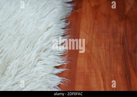 Eine extreme Nahaufnahme der Kante eines flauschigen Weißer Teppich auf einem Holzboden Stockfoto