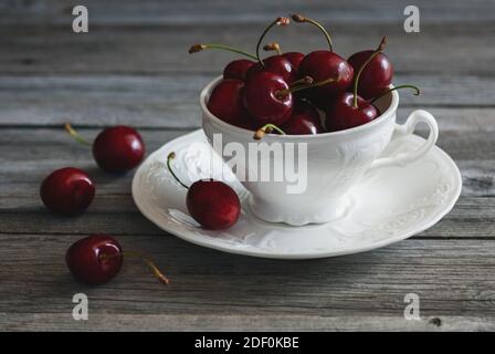 Rote Kirschen in weißer Teetasse auf gealtertem Holzhintergrund, Fruchtstillleben Stockfoto