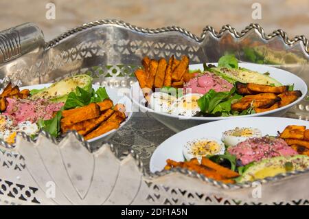 Saftige Salatschüsseln mit Avocado, Süßkartoffeln, Rucola und Samen auf silbernem Tablett im Freien Stockfoto