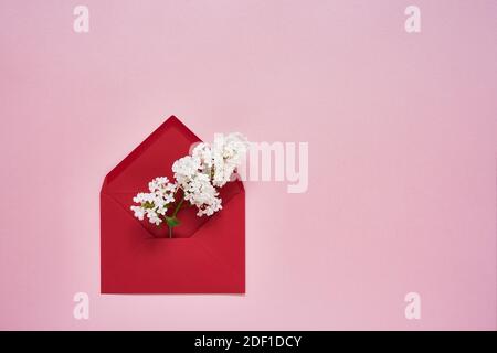 Weiße Fliederblumen in rotem Umschlag auf rosa Pastellhintergrund. Flat Lay of Birhday, Mothers Day, Bachelorette, Hochzeitskonzept. Platz kopieren, Draufsicht Stockfoto