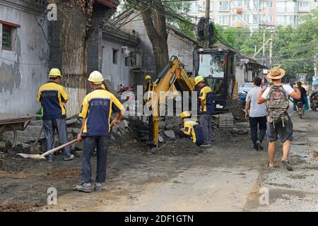 Ein Team von Arbeitern steht wieder auf einer Hutong-Straße im westlichen Zentrum von Peking, China, während Fußgänger vorbei gehen. Stockfoto