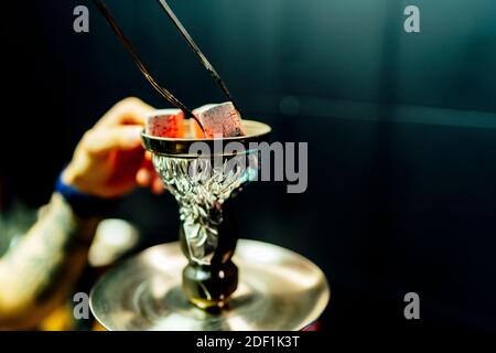 Kellner platziert rauchenden Holzkohlesteinen für Shisha Stockfoto