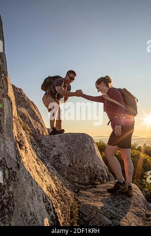 Afroamerikanischer Mann hilft weiblichen Wanderer auf Kante auf Berg In Maine Stockfoto