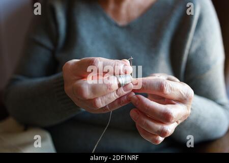 Alte Frau, die eine Nadel einfädelte Stockfoto