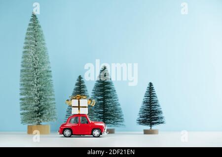 Weihnachten rotes Auto mit einer Geschenkbox in einem Kiefernwald. Leerzeichen für Text. Happy New Year Card Konzept Stockfoto