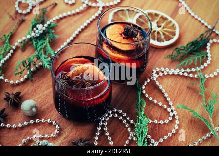 Zwei Gläser Glühwein mit Zitrusfrüchten, Sternanis, Muskatnuss auf Holztisch. Weihnachtliches Glühgetränk, Neujahrsdekoration, Draufsicht. Stockfoto