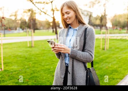 Glücklich lächelnde Frau mit Telefon auf der Straße der Stadt. Vor dem Hintergrund eines schönen Sonnenuntergangs Stockfoto